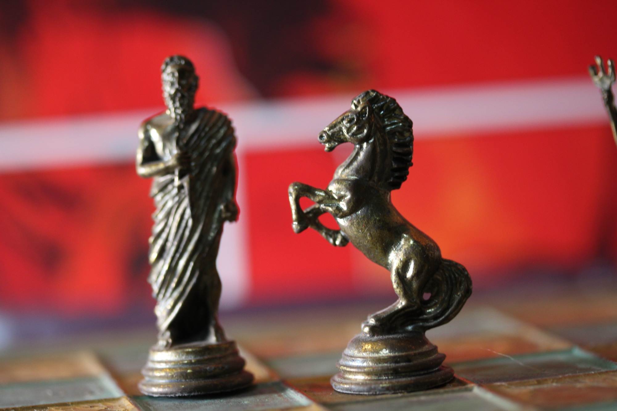 Closeup of Greek mythology chess pieces on the board with a red blurry background